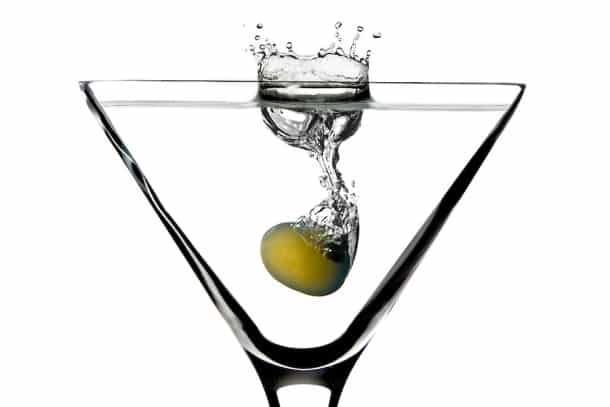 Single green olive splashing into Martini glass