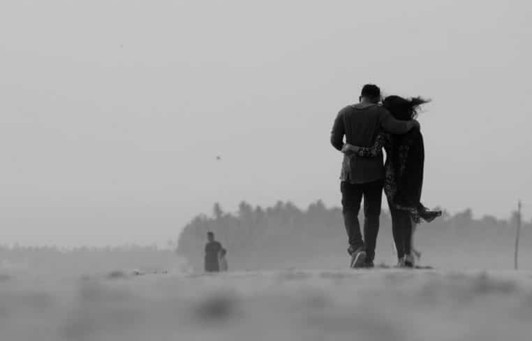 A romantic black and white shot of a couple walking arm in arm on a misty beach in Kochi, India.