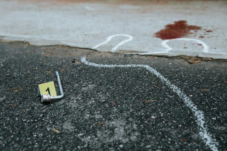 Crime scene showing chalk outline and evidence marker on asphalt.