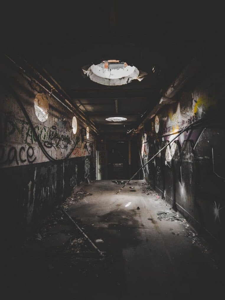 Discover the eerie charm of an abandoned hallway adorned with graffiti and light peeking through.