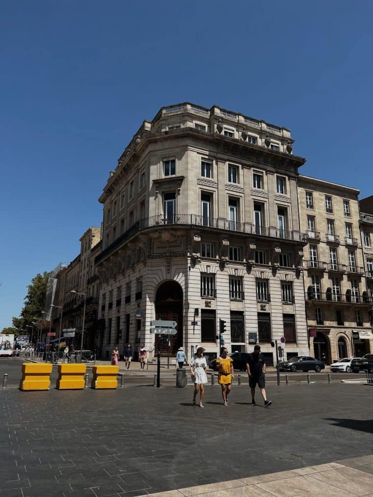 A bustling street view of Bordeaux showcasing historic architecture under a clear blue sky.