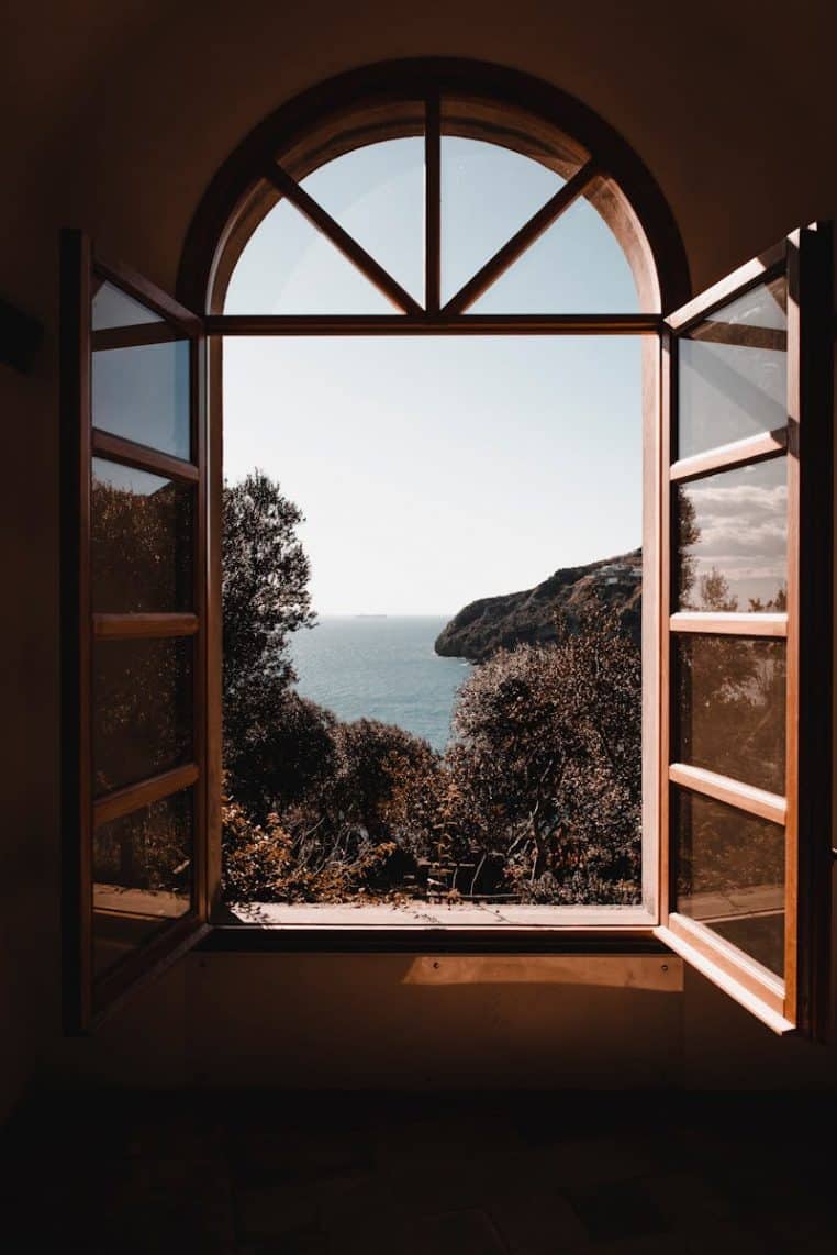 Elegant arched window view of a serene ocean landscape with lush greenery.