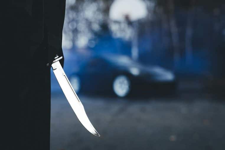 Close-up of a knife with a blurred car in the background, creating a tense atmosphere.