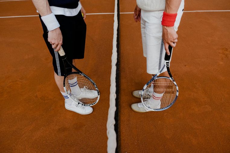 Two tennis players stand on a clay court with rackets, ready for a match.