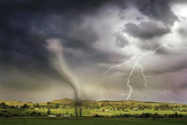 A powerful tornado and vibrant lightning striking over a rural countryside landscape.