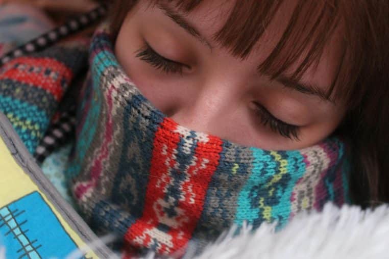 Woman resting with eyes closed, wrapped in a warm, colorful wool scarf, depicting comfort and warmth.