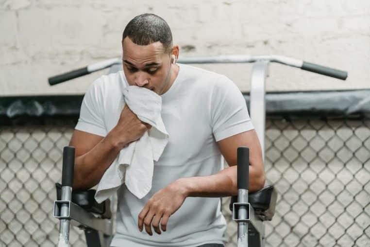 Serious African American male wiping face with towel during abdomen exercises on stand in modern gym
