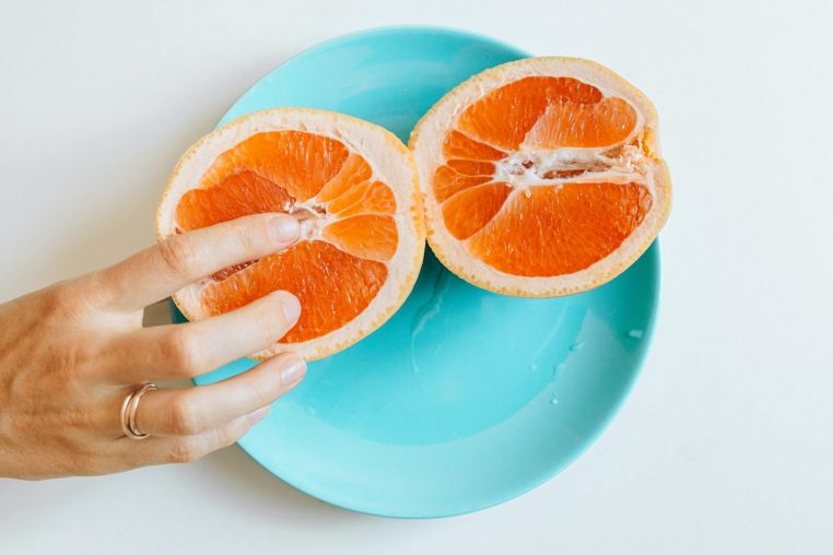A grapefruit sliced in half on a plate, touched by a hand, symbolizing sensuality and education.